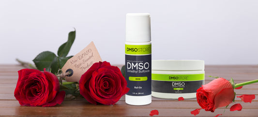 DMSO rose-scented roll-on and gel on wood counter with roses and a tag that says "New DMSO Rose-Scented Products"