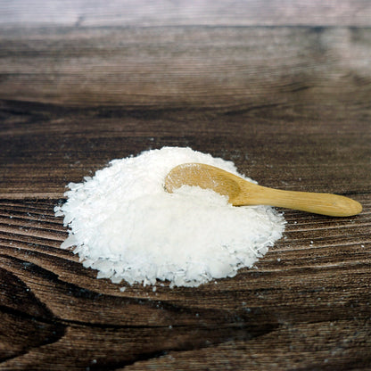 Stearic acid flakes on a bamboo spoon on a wooden table, highlighting natural product for eco-friendly cleaning.